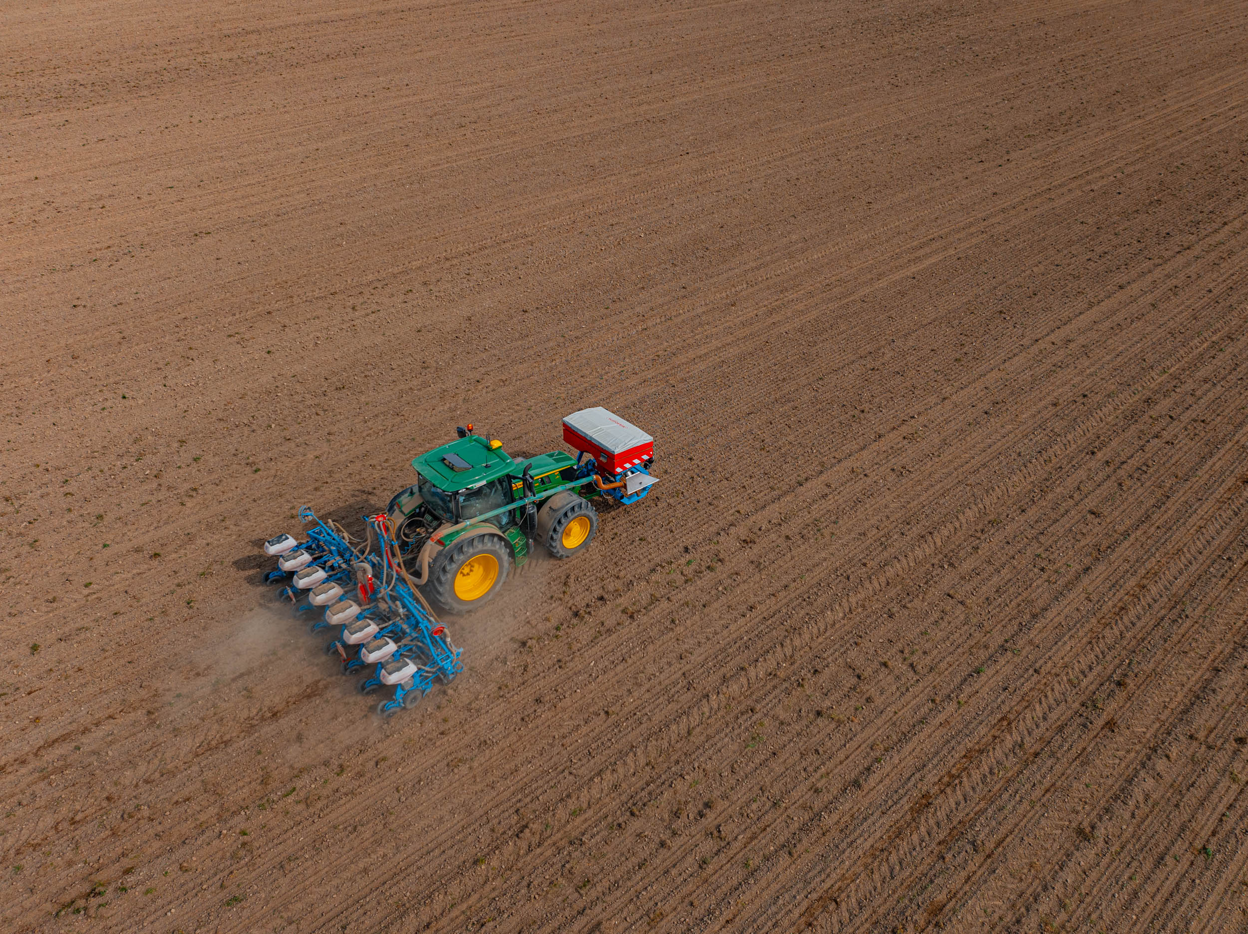 Drohnenaufnahme eines Traktors mit Sämaschine bei der Aussaat auf einem großen Feld – präzise landwirtschaftliche Dienstleistungen von Ostermaier.