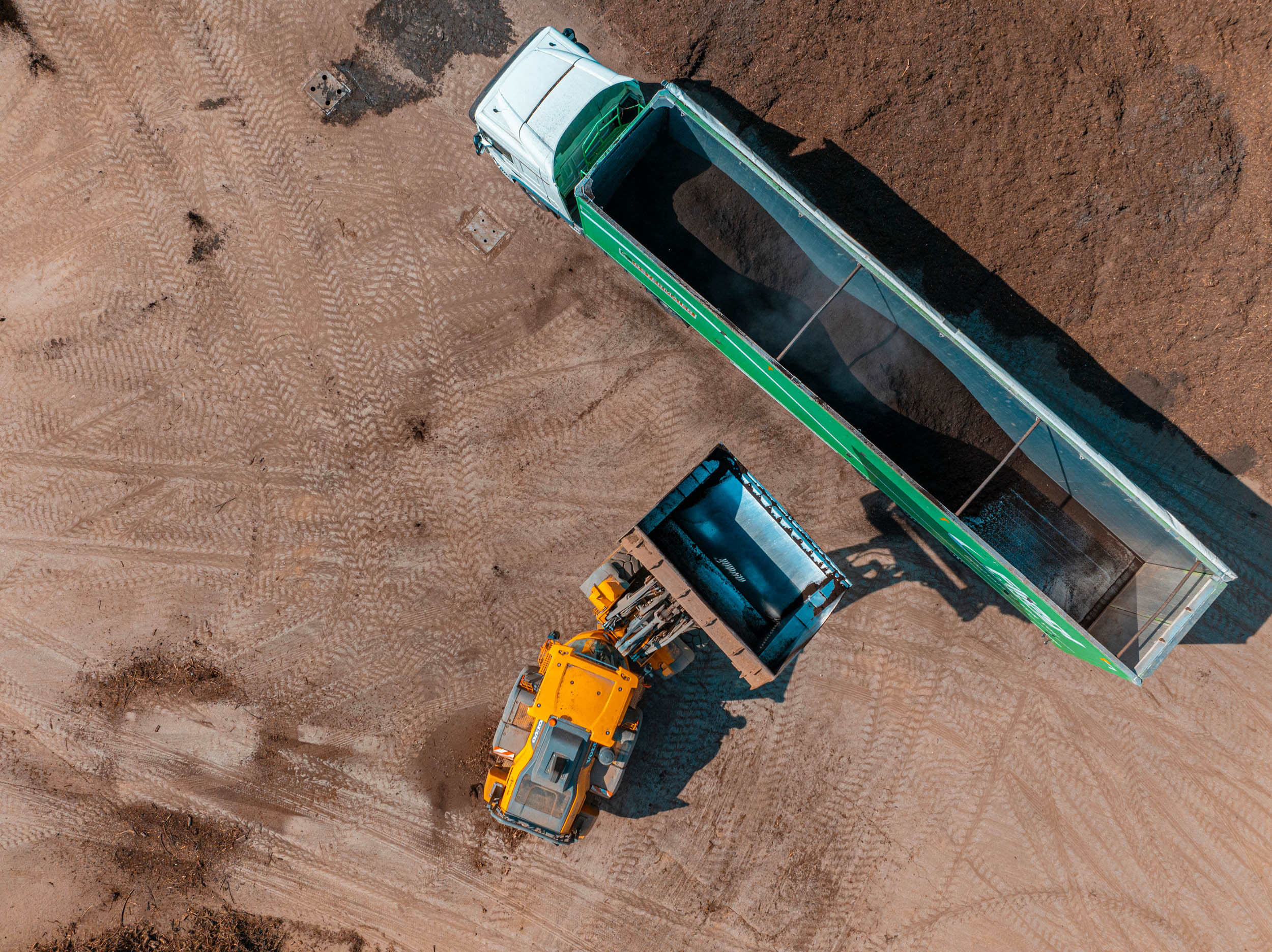 Radlader belädt einen großen LKW mit Kompost oder Erde – Ostermaier Dienstleistungen, professionelle Transporte von Schüttgütern.